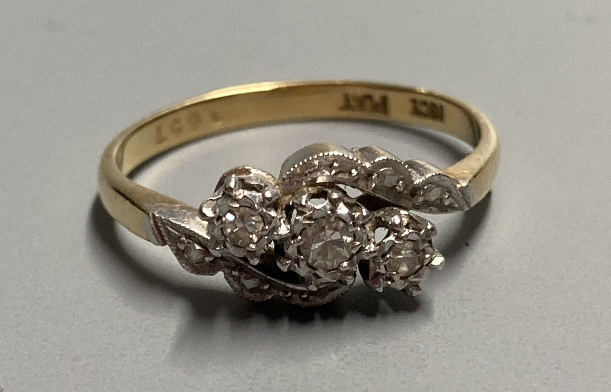 An 18ct and plat. illusion set three stone diamond crossover ring, size O/P, gross 3 grams.